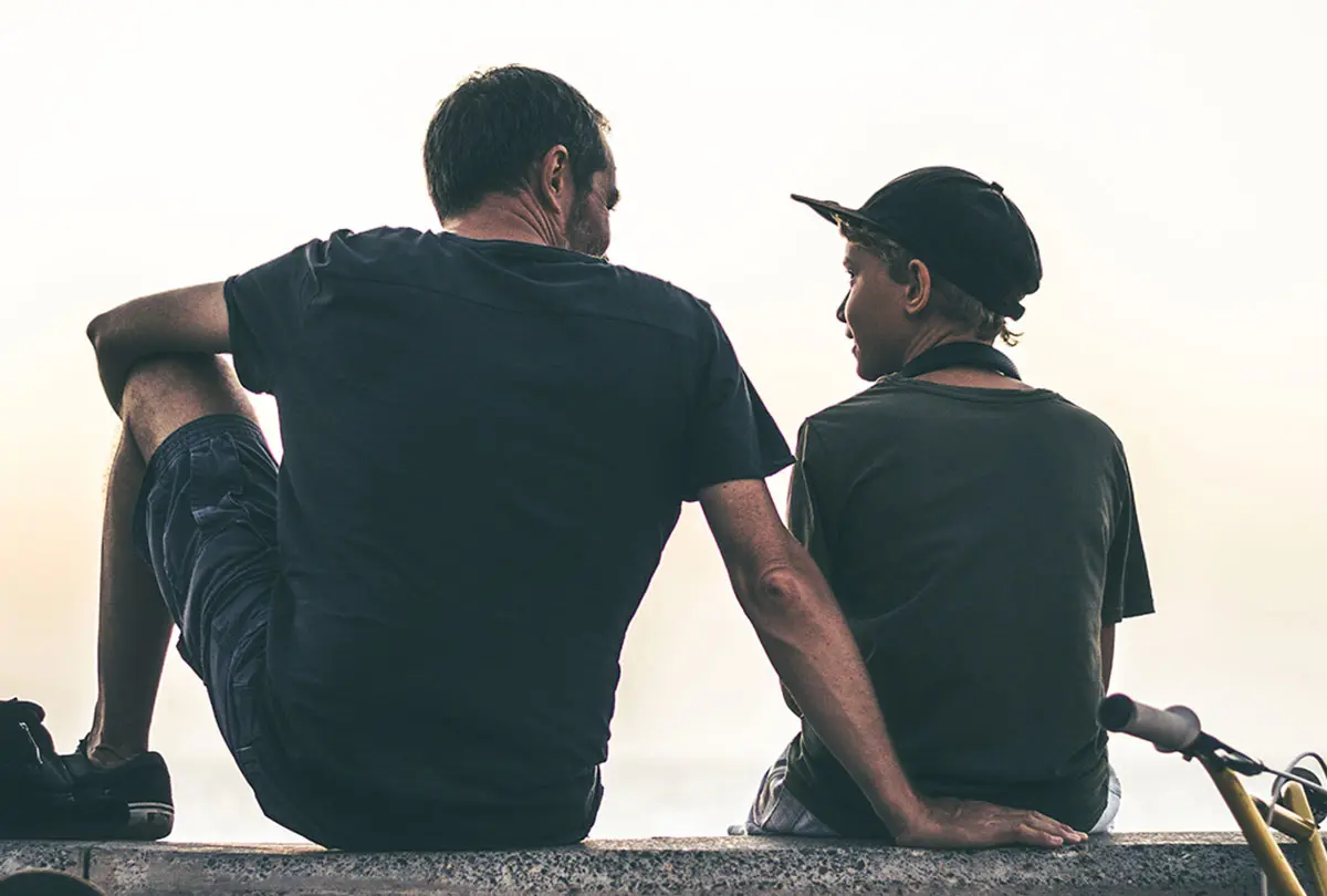 A man and a boy sit together on a ledge, enjoying a moment of companionship and conversation.