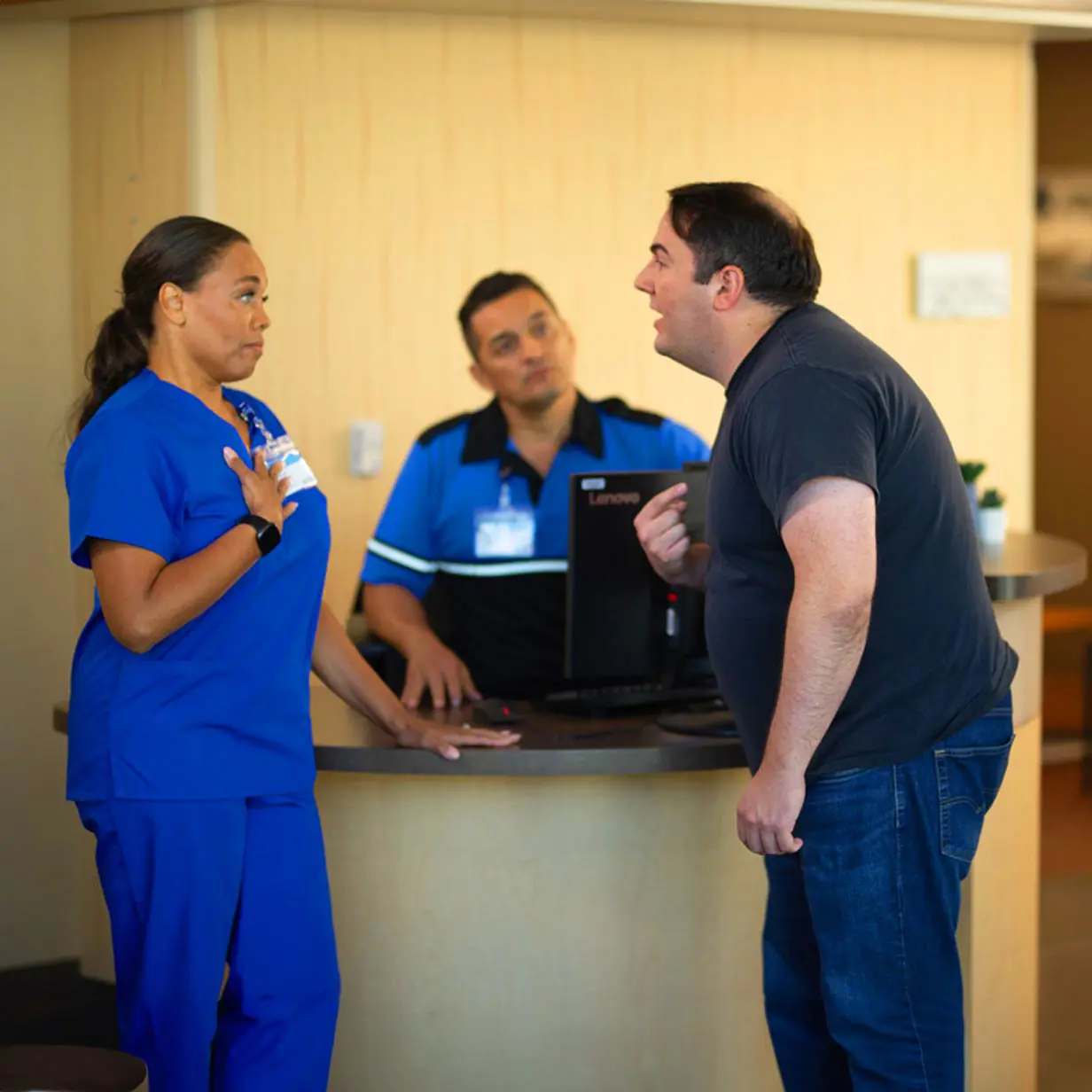 An angry man talking to a medical professional at a security desk.