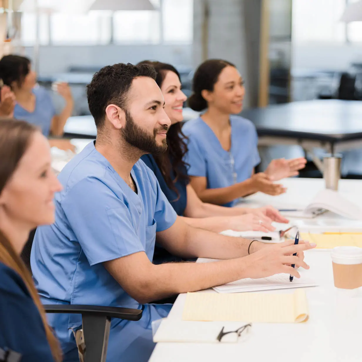 A group of medical professionals sitting at table listening to someone speak.